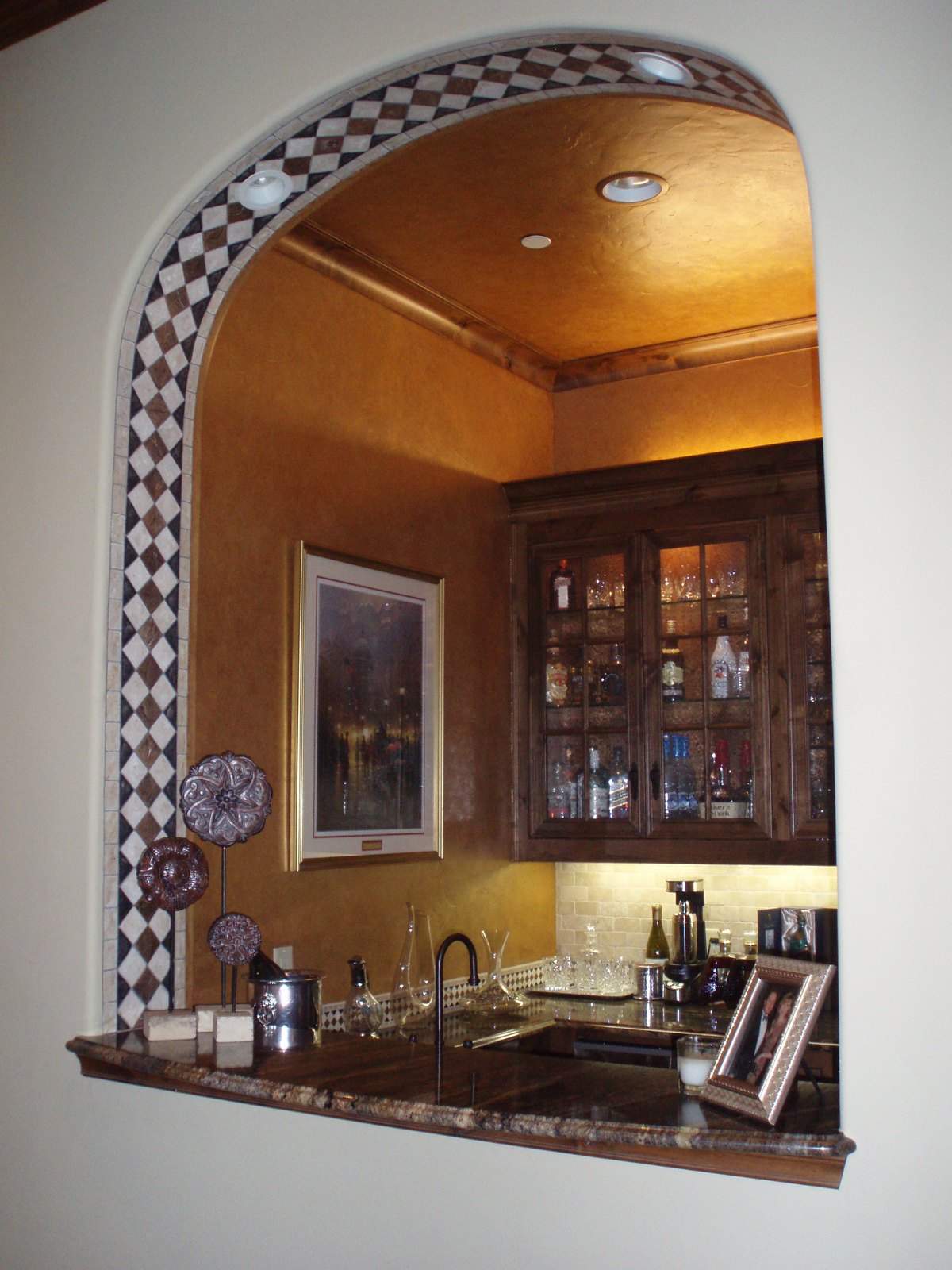 The same arch rebuilt as a wet bar with granite counter, glass-front cabinets and a mosaic tile surround