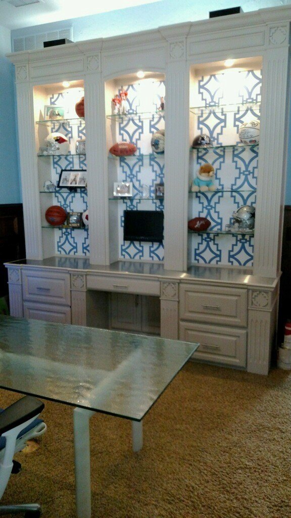 The same built-in painted pale, with patterned wallpaper backing and lit glass shelves