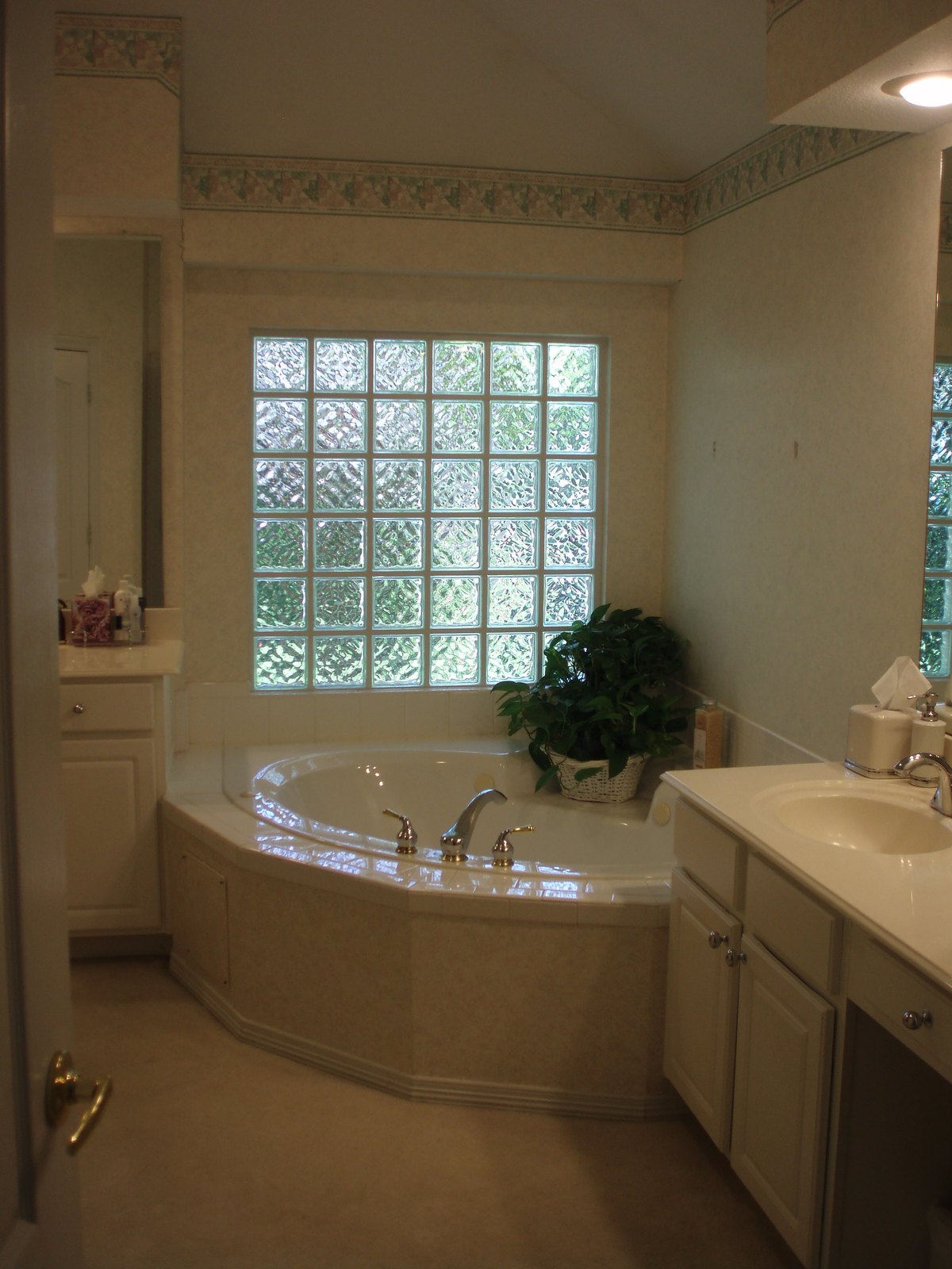 Dated master bathroom with a corner tub, glass block window and cream tile