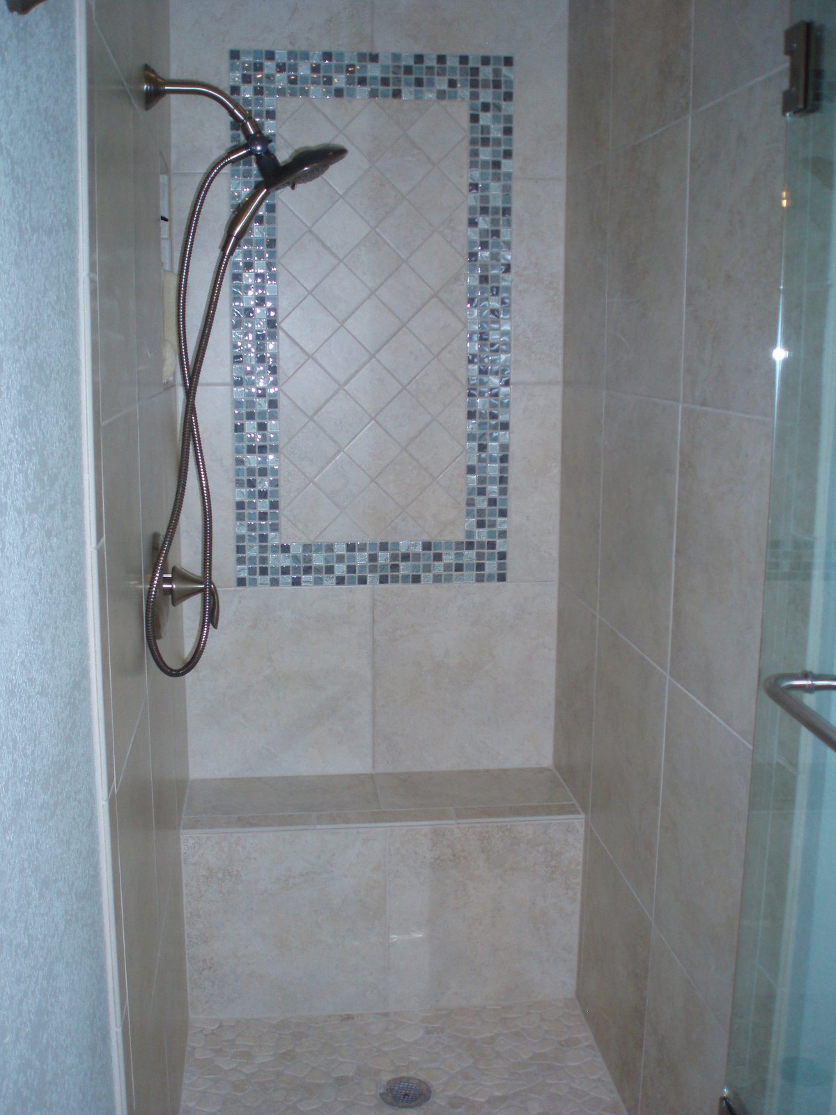 The same alcove rebuilt as an open tiled shower with a mosaic inset panel and a bench