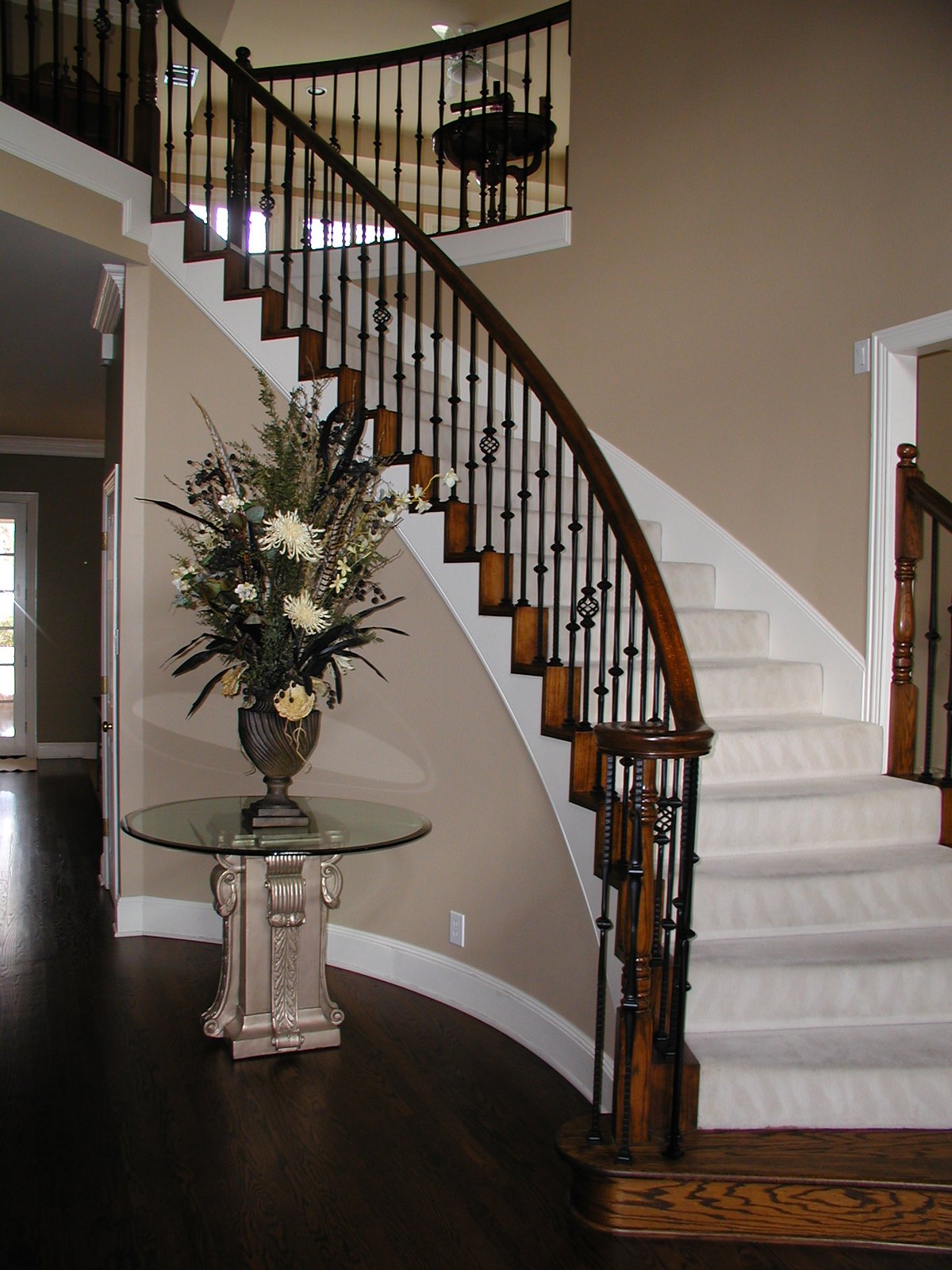 The same staircase with dark wrought-iron balusters, a dark stained rail and hardwood floors