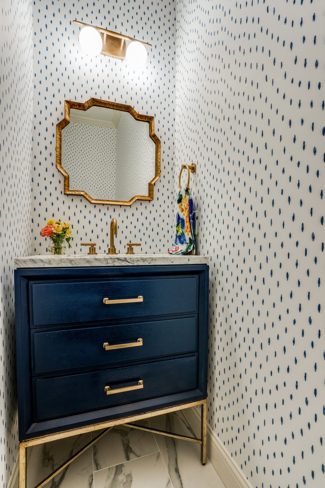 Powder room with a navy chest vanity, brass mirror and dotted wallpaper