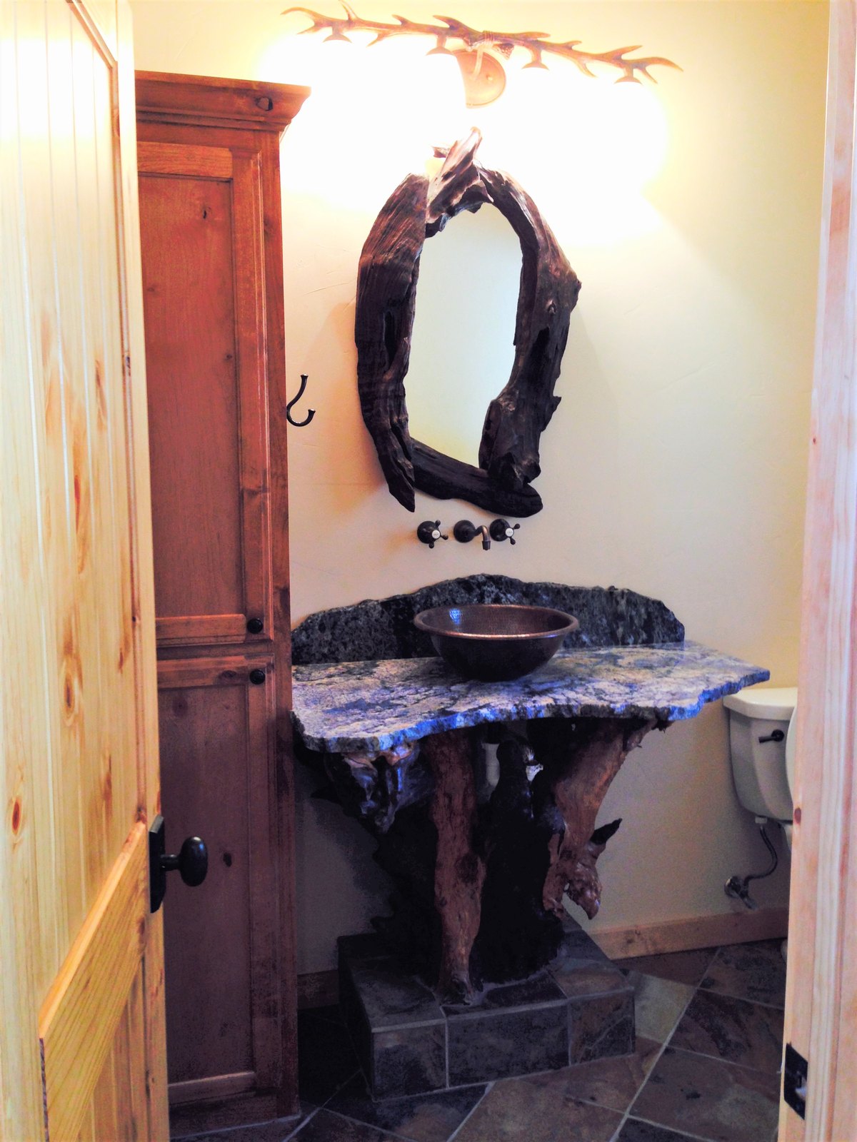 Rustic powder room with a stone vessel sink on a driftwood base and antler sconce