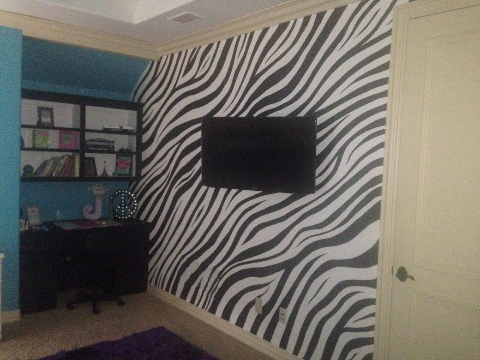Bedroom with a zebra accent wall, teal walls and a wall-mounted television