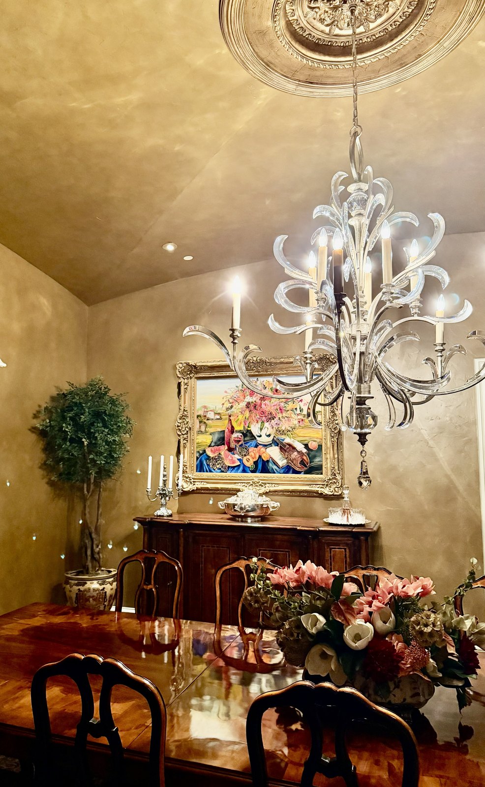 Dining room with a hand-blown glass chandelier, gilded mirror and a large floral arrangement
