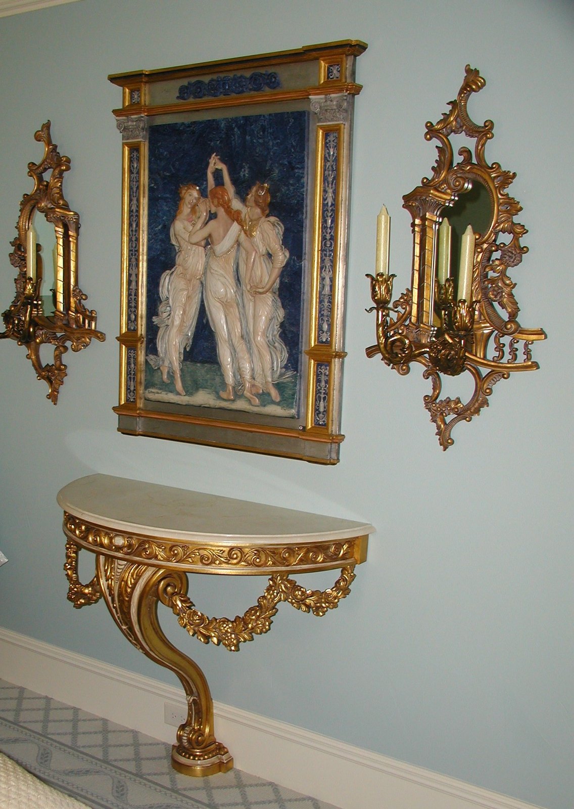 Gilded console beneath a classical painting with sconces