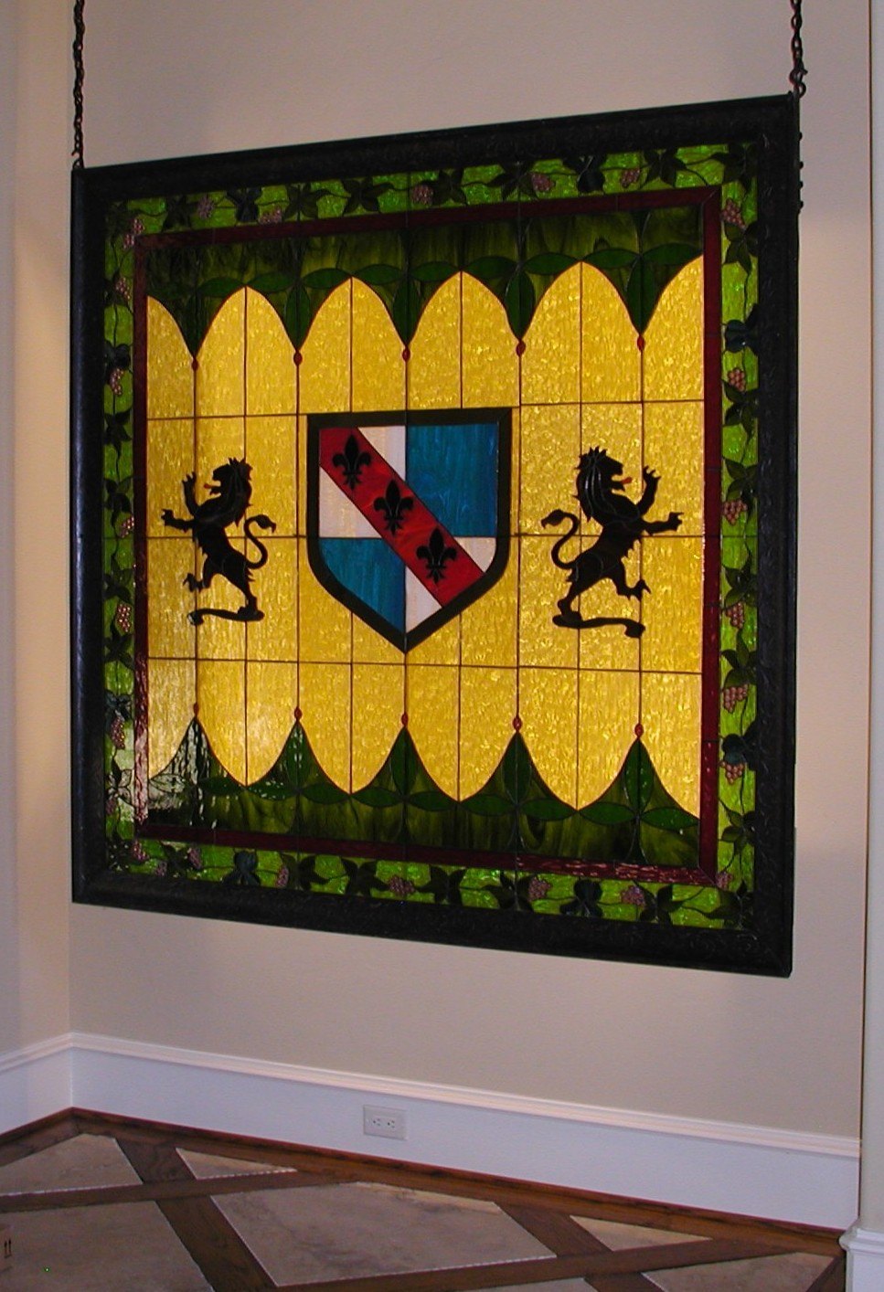 Heraldic stained glass panel with lions and a shield, designed by Jan Revels and hung in a window