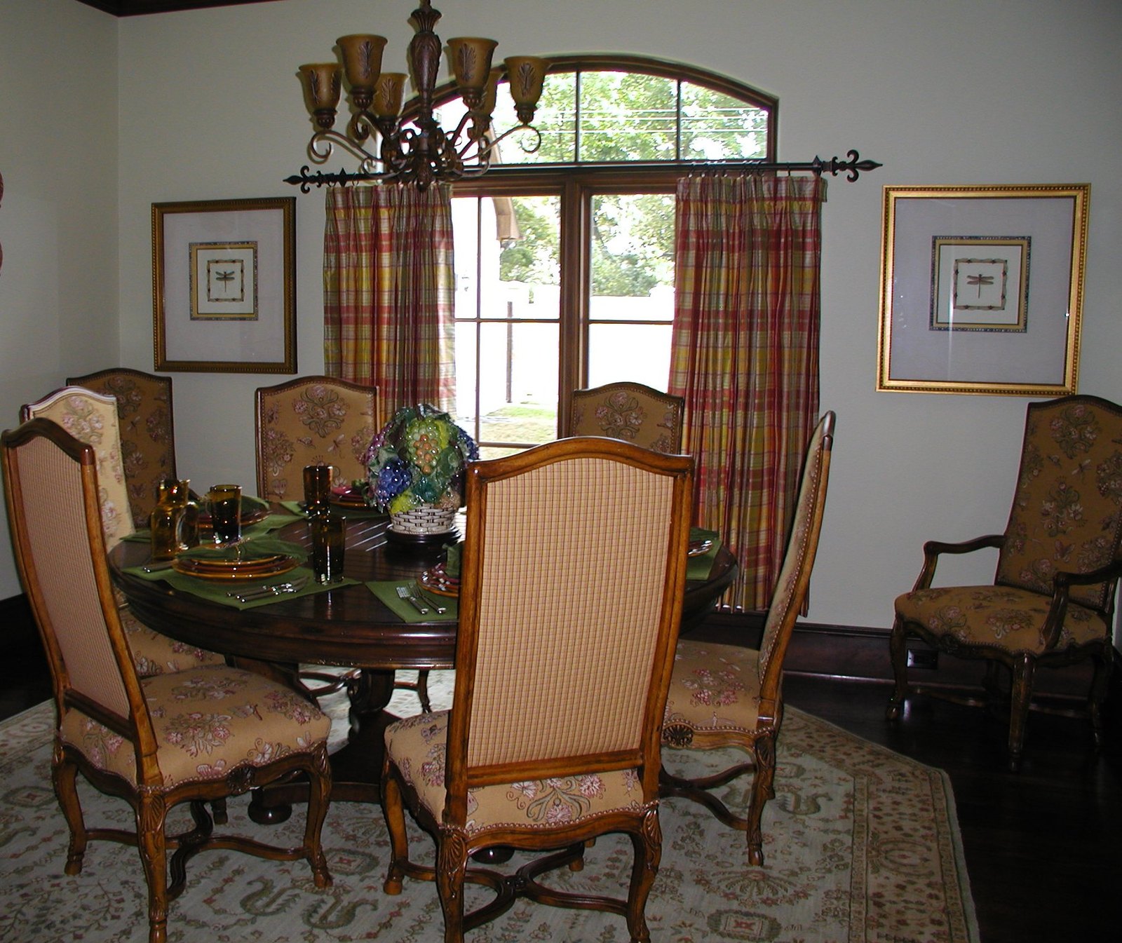 Round dining table with plaid drapes, tapestry chairs and a glass centrepiece