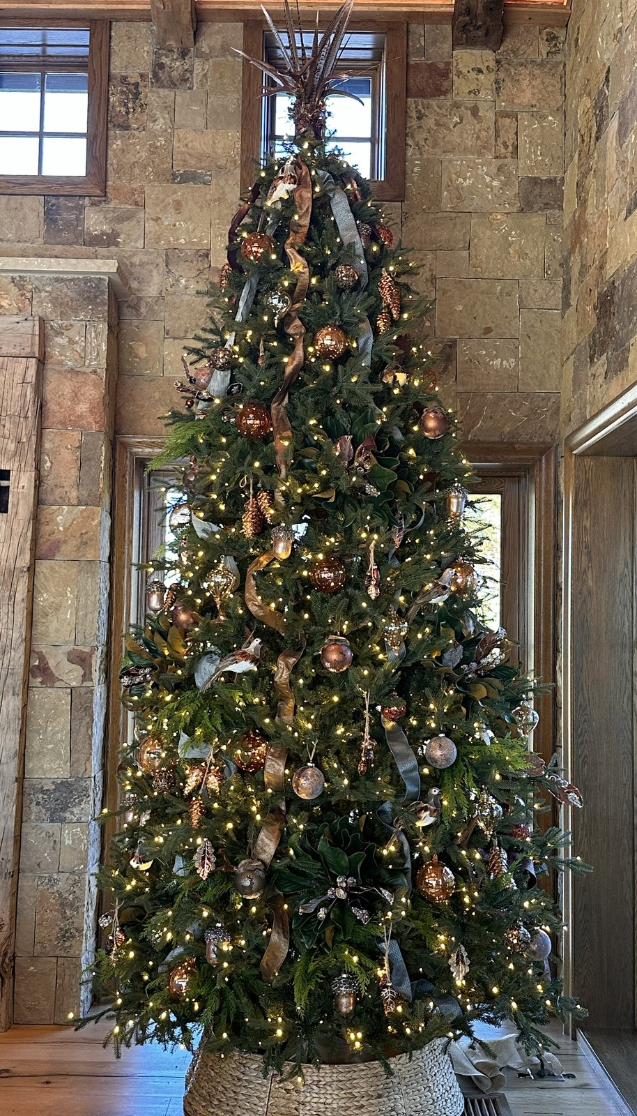 Tall Christmas tree in copper and gold against a stone wall in a double-height room