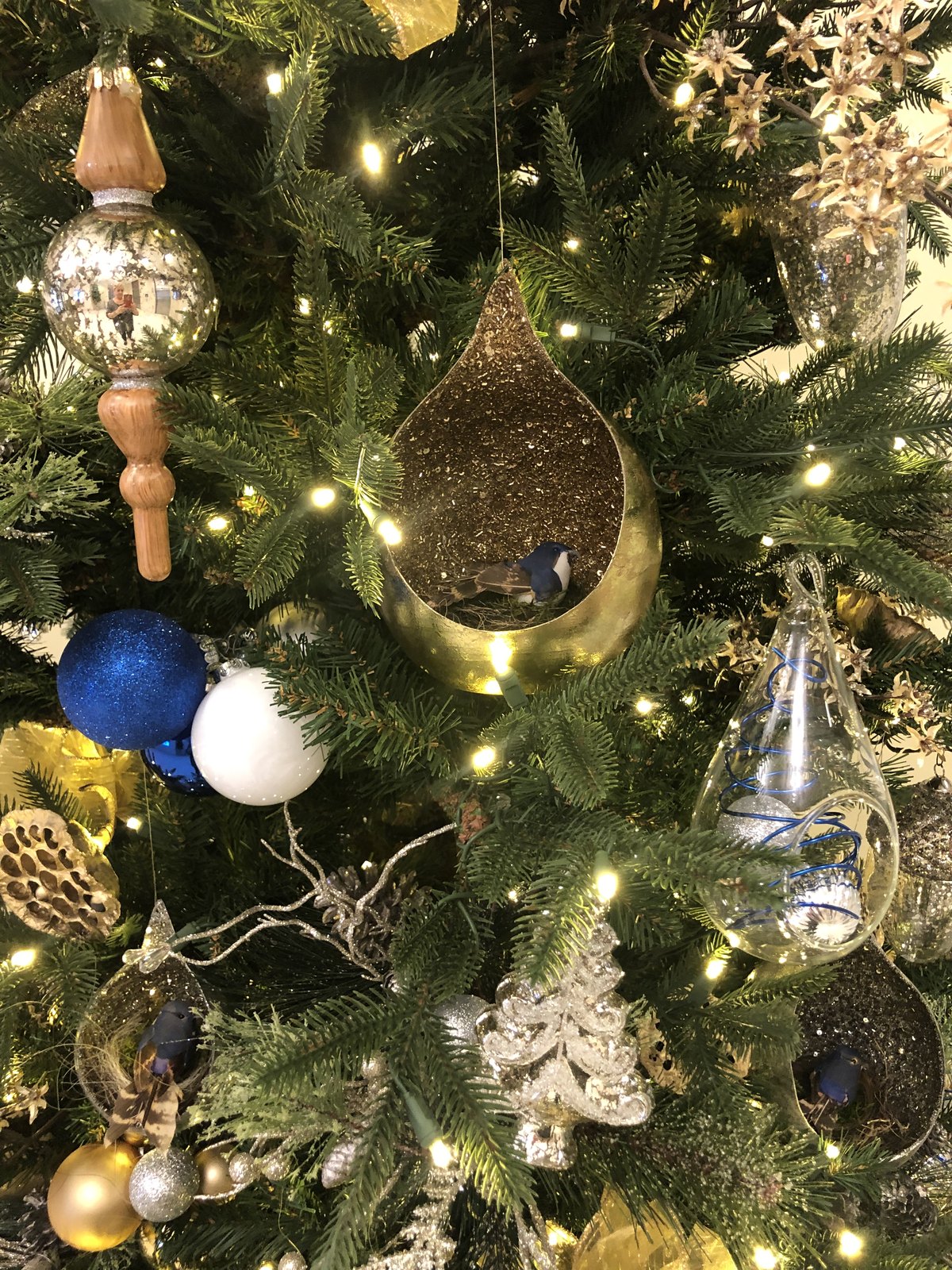 Close view of gold, silver and blue woodland ornaments on a lit Christmas tree