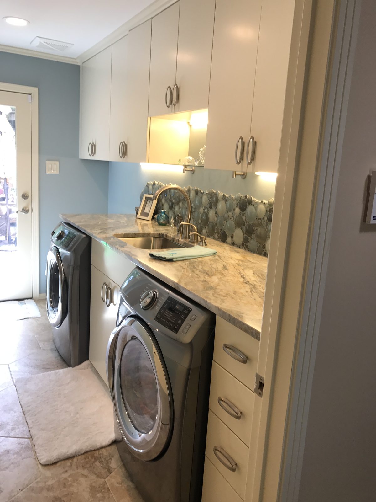 Renovated laundry room with cabinetry, counter and stacked appliances