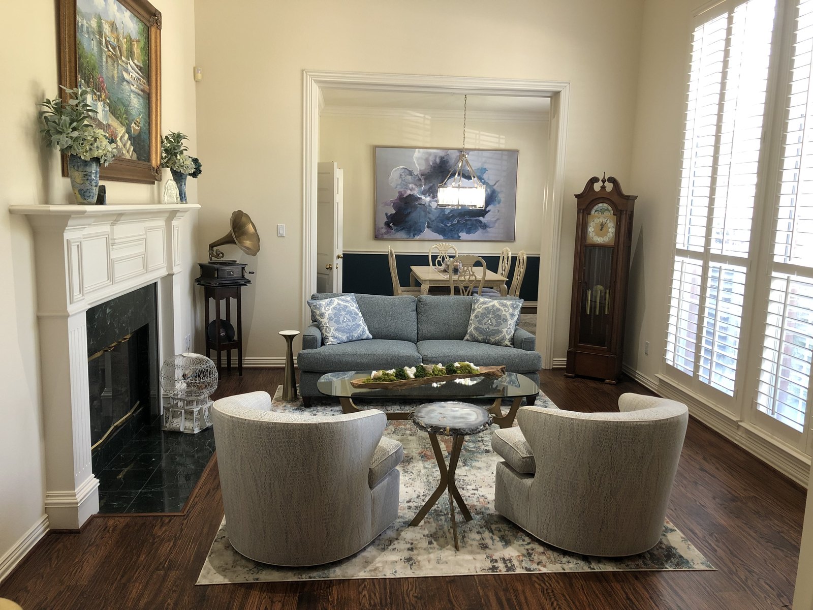 Living room with a white fireplace, blue sofa and cream swivel chairs opening to the dining room